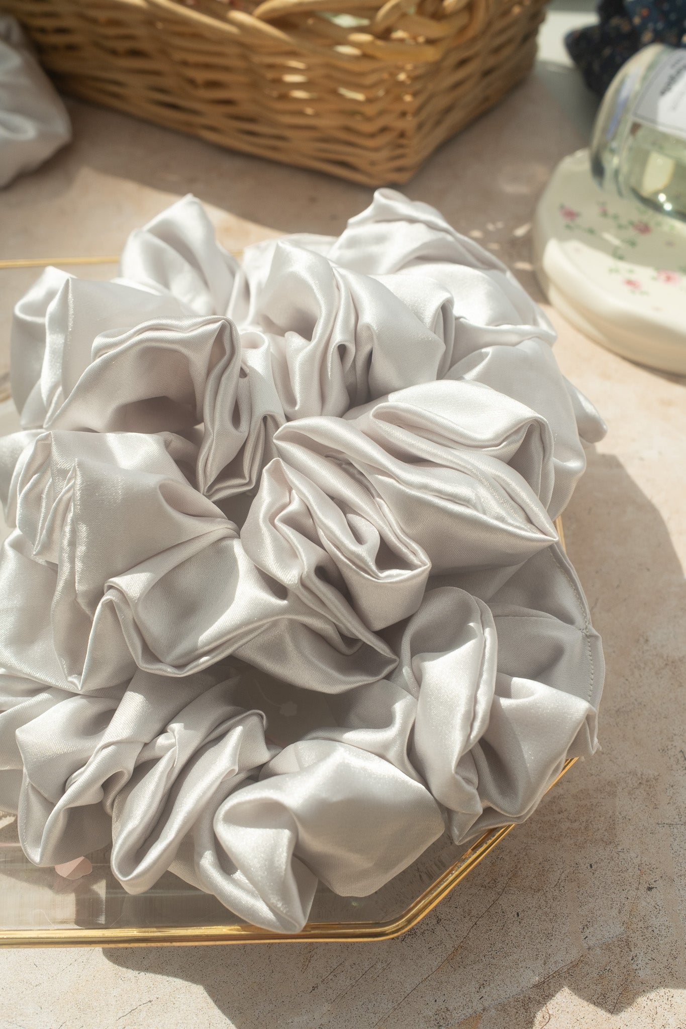 White satin scrunchie on a textured surface with a basket in the background