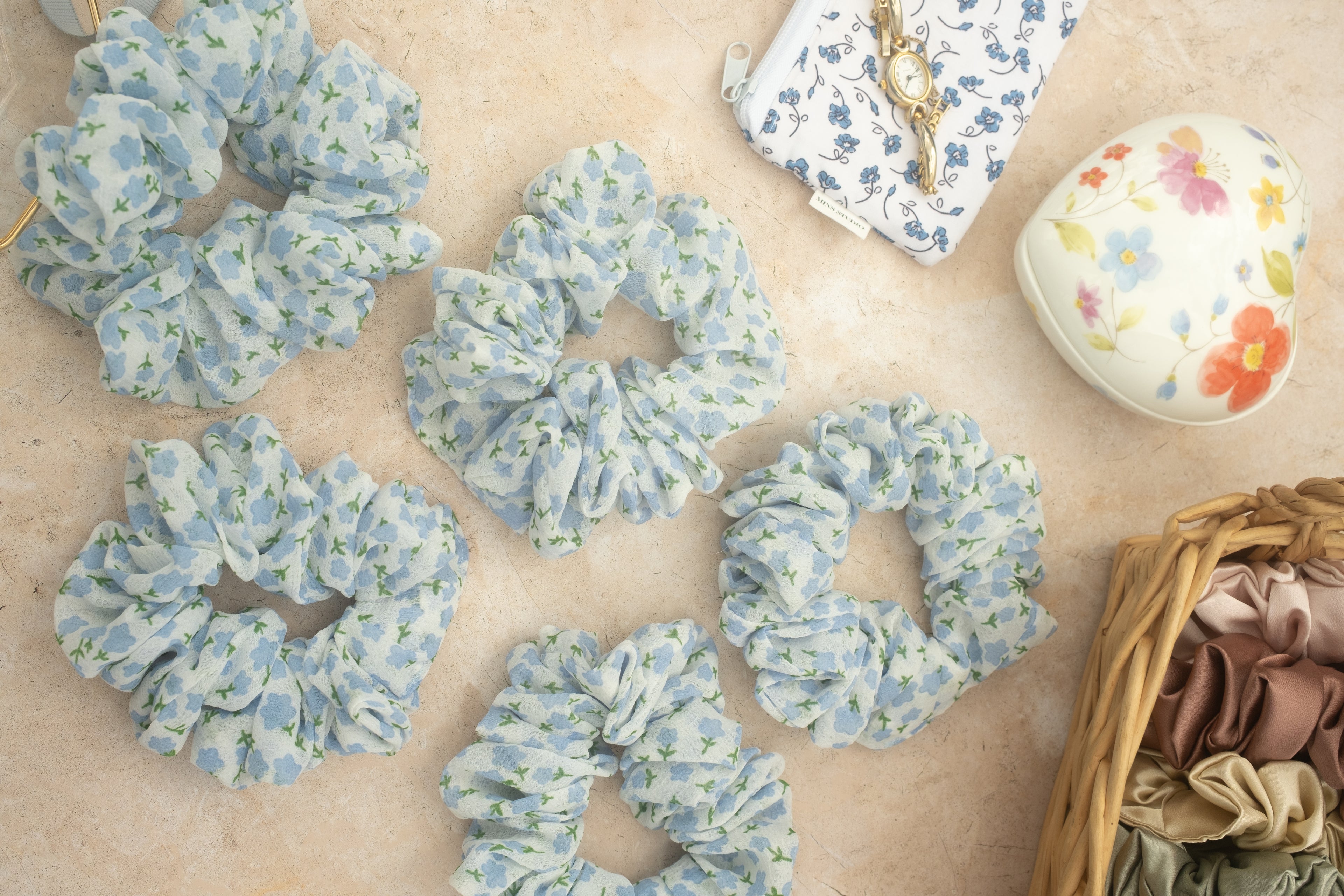 Floral scrunchies on a textured surface with a small basket of additional scrunchies.