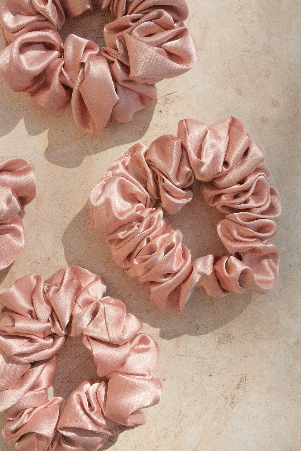 Pink satin scrunchies on a textured beige surface