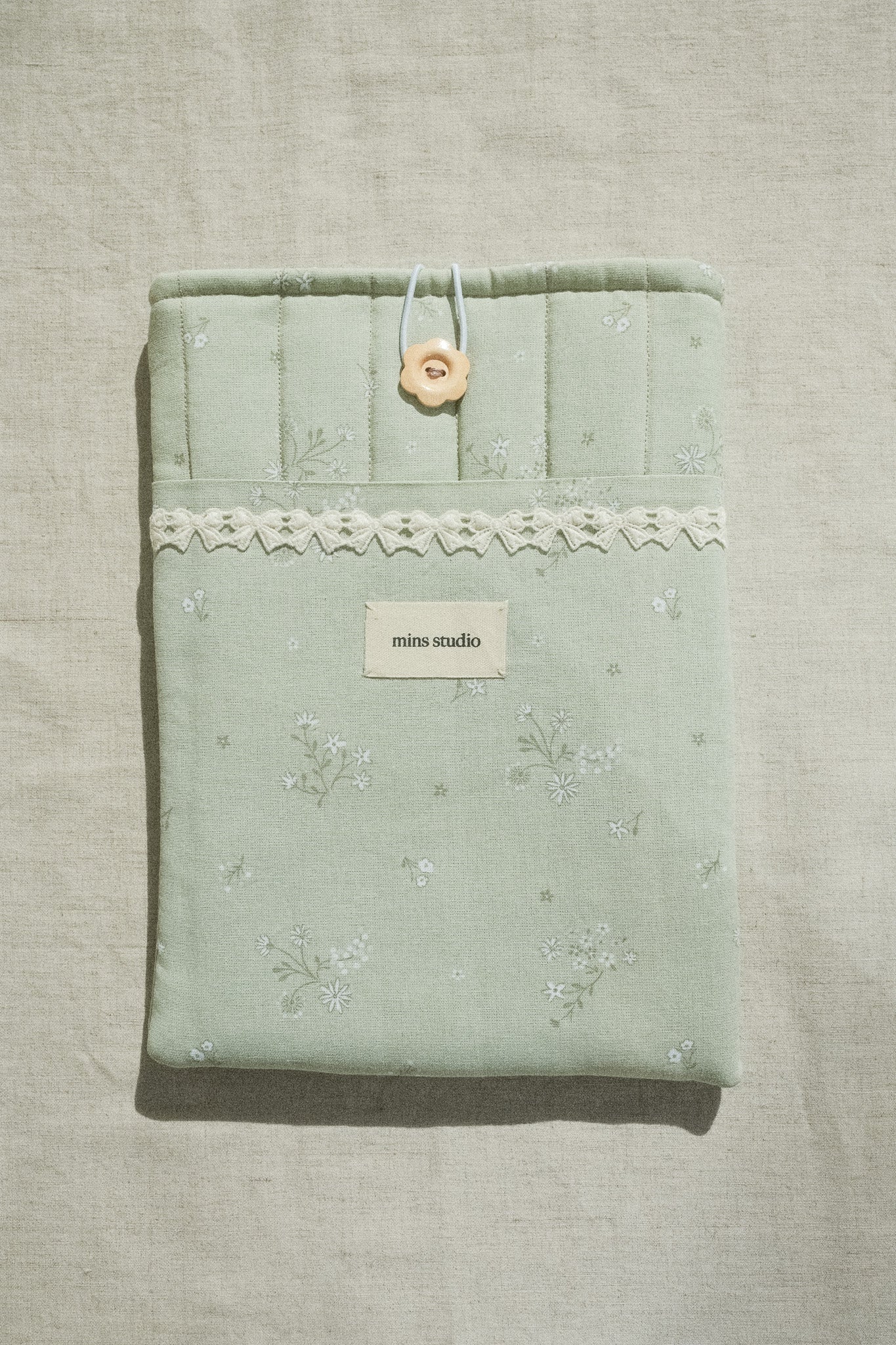 Green fabric booksleeve with lace details on a textured beige background