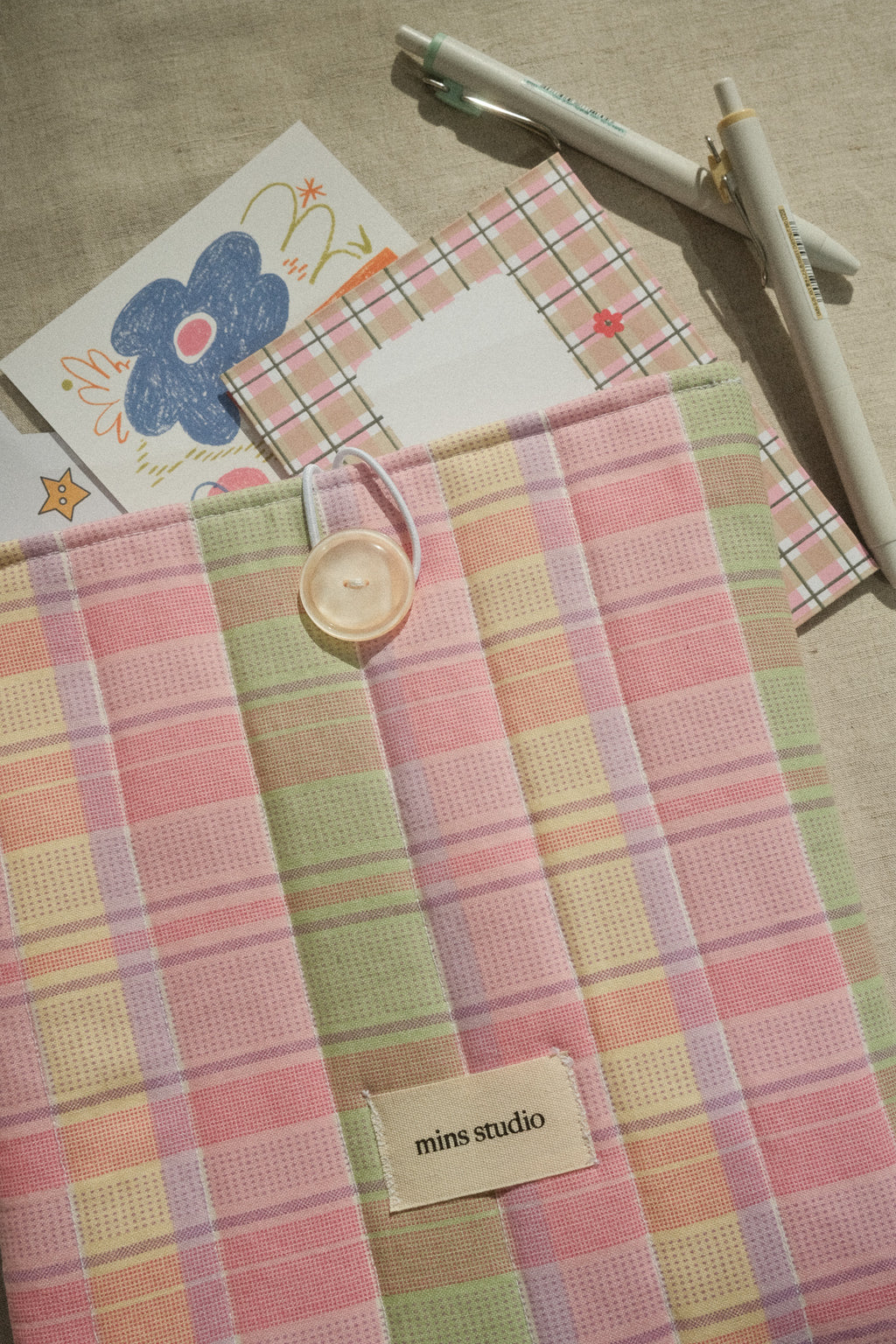 Pastel checkered book sleeve with a button, card, and pen on a textured surface