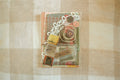Packaged decorative items with lace and vintage-style packaging on a checkered fabric background
