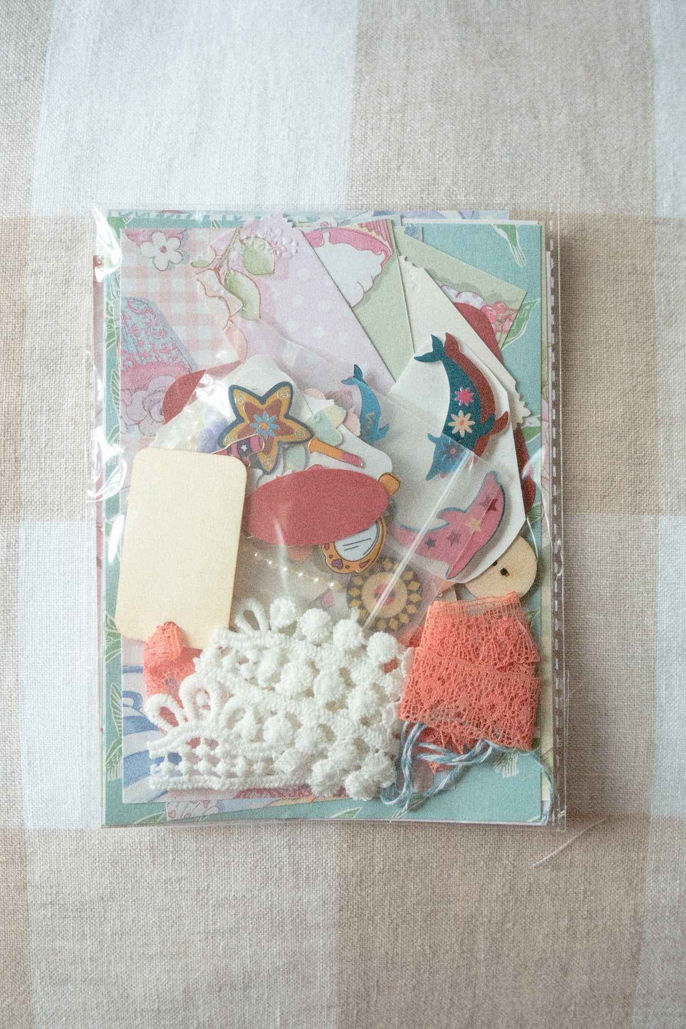 Set of decorative paper pieces and embellishments in a clear plastic package on a beige surface.