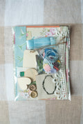 Collection of decorative items including a necklace, flowers, and ribbons on a checkered fabric background.