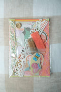 Packaged craft supplies including scissors, thread, and decorative elements on a textured surface.