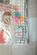 Decorative stationery set with ribbons, buttons, and a 'Make a Wish' tag on a neutral background.