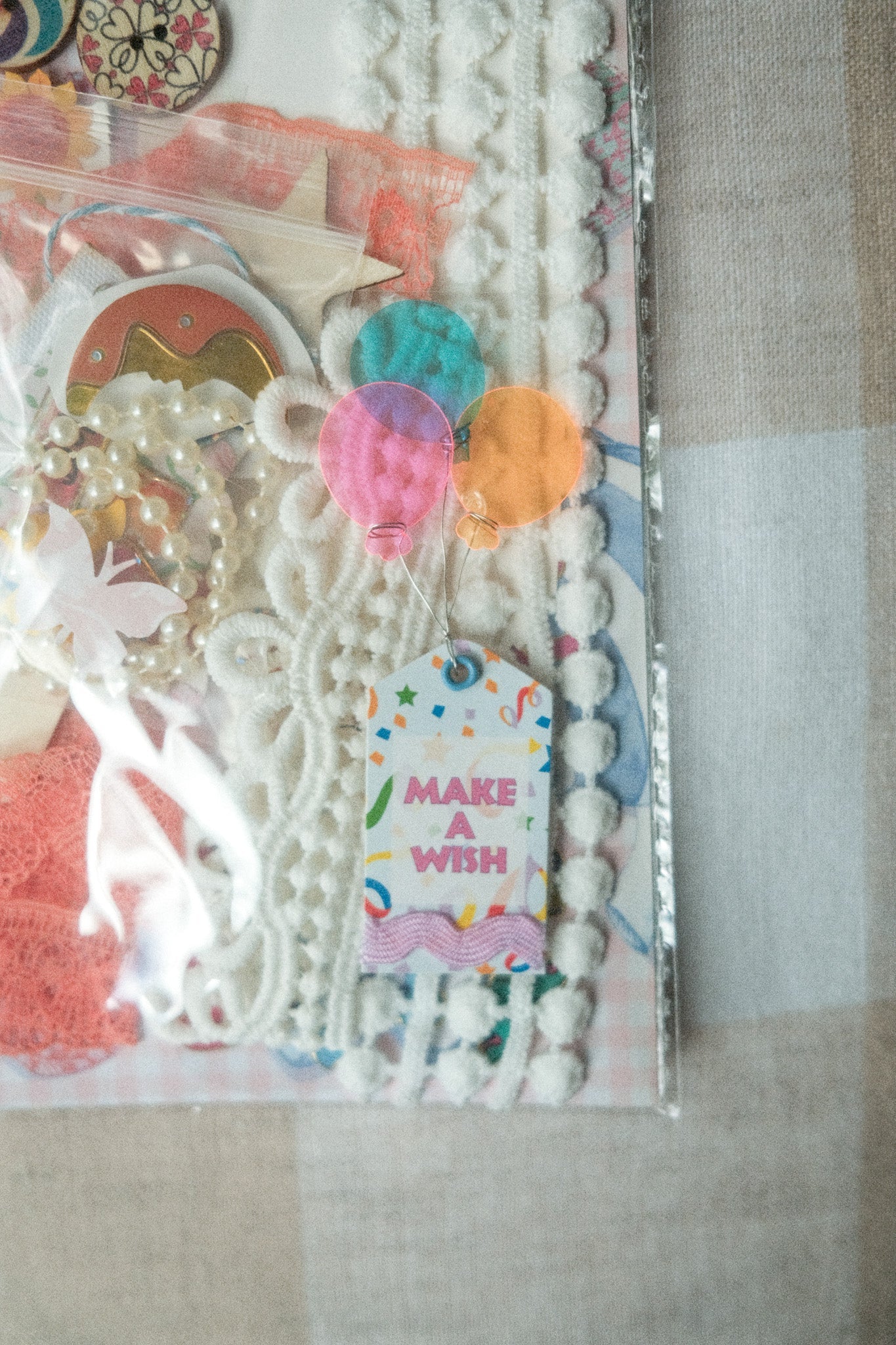Decorative stationery set with ribbons, buttons, and a 'Make a Wish' tag on a neutral background.