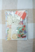 Packaged craft supplies including buttons and beads on a checkered fabric background