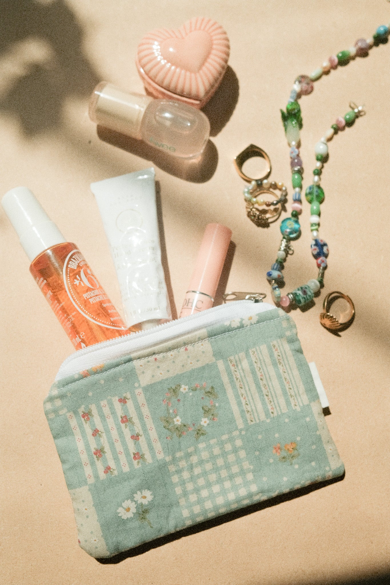 Small pouch with cosmetic items and jewelry on a beige surface