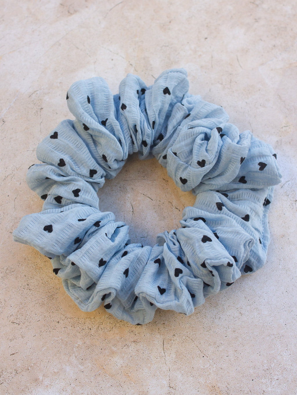 Blue scrunchie with black heart patterns on a beige surface