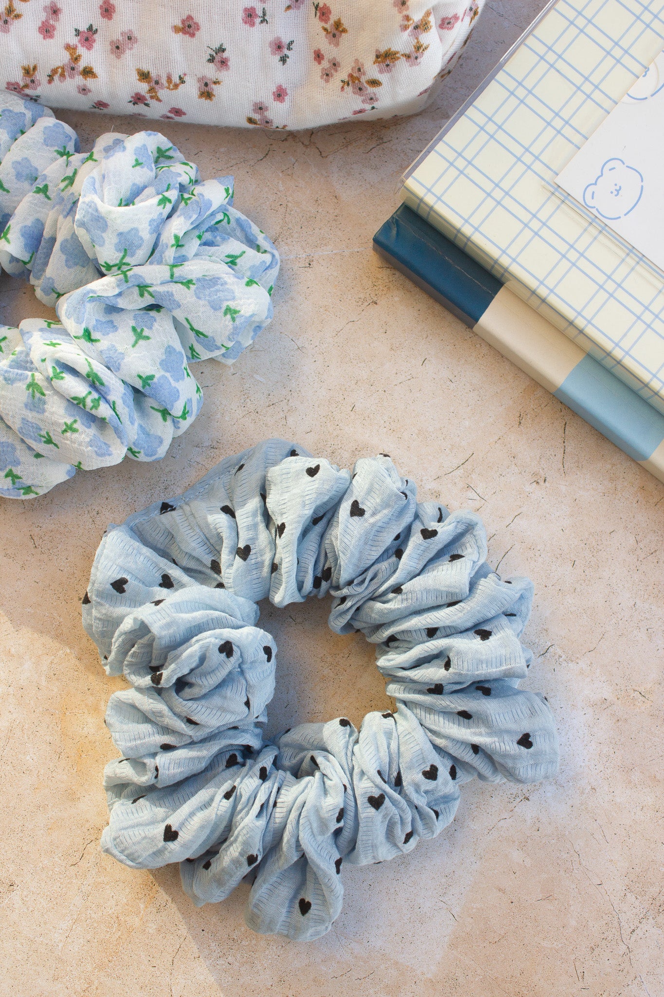 Blue scrunchies with floral patterns on a textured surface with a notebook.