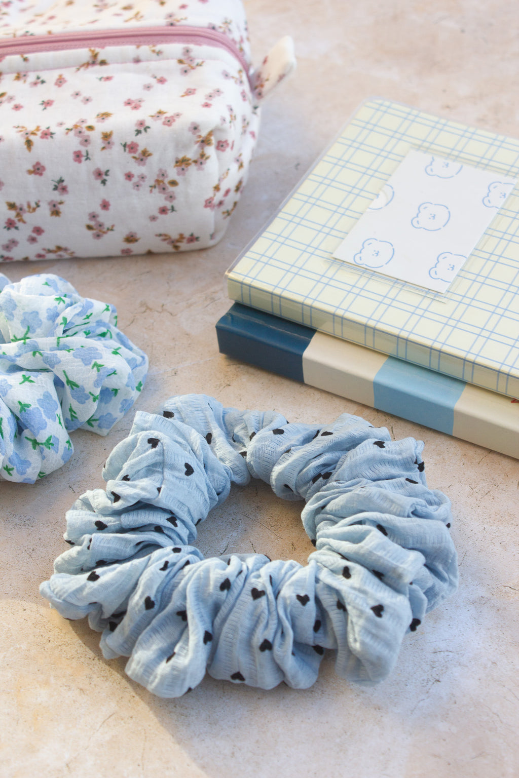 Blue scrunchie with black polka dots on a light surface with a floral pouch and notebook in the background.