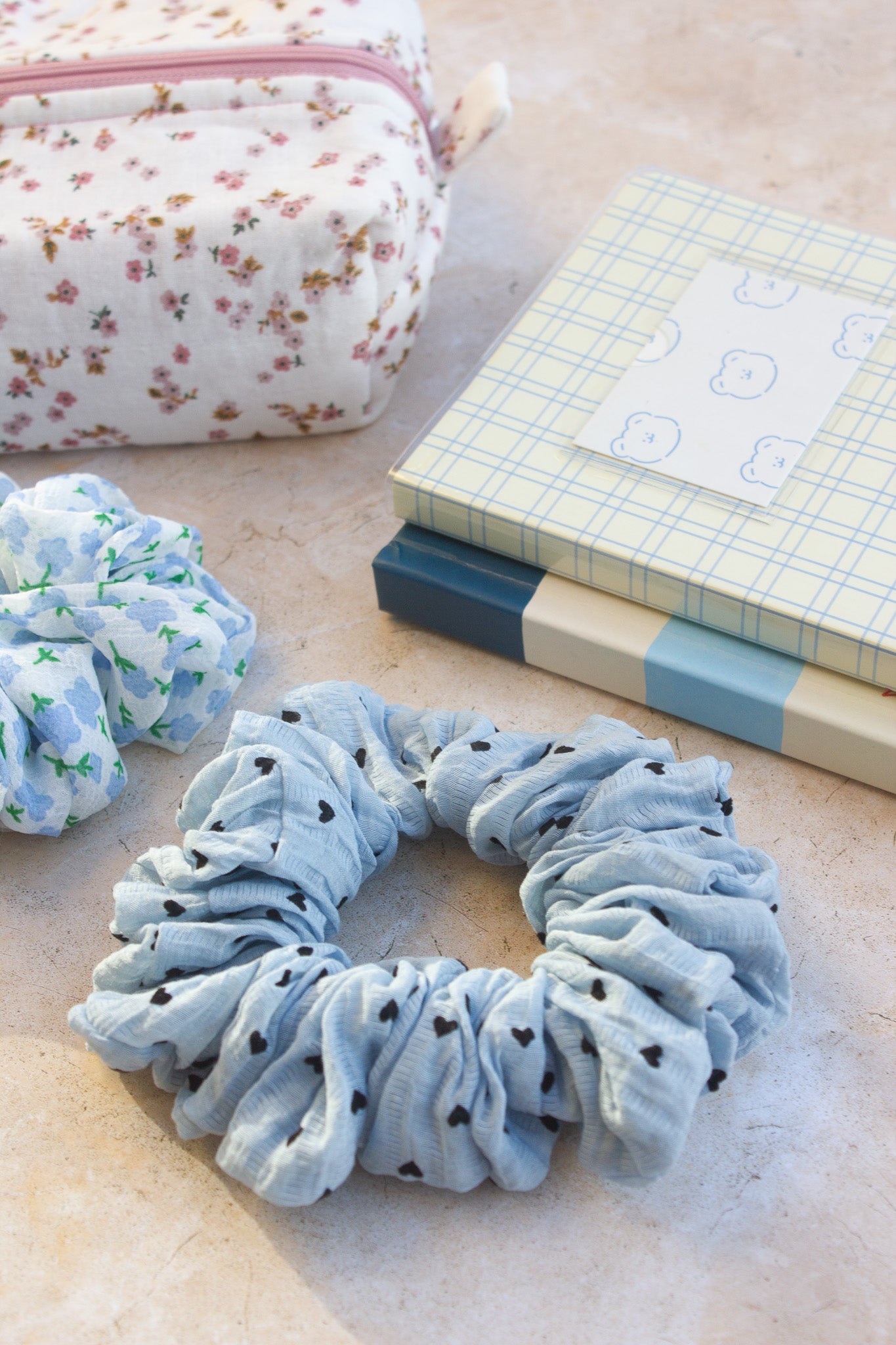 Blue scrunchie with black polka dots on a light surface with a floral pouch and notebook in the background.
